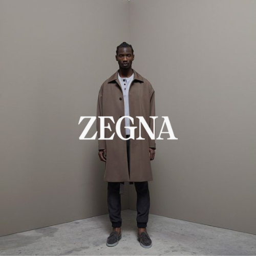 Zegna Kollektion – Model luxuriös gekleidet mit Loafers, Mantel und langer Hose steht auf grauem Boden vor neutraler Wand, eleganter Lifestyle bei Closory