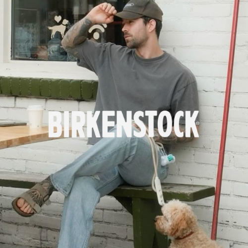 Birkenstock Kollektion – Model in Sandalen, Jeans und T-Shirt vor weißem Café, lässiger Lifestyle bei Closory