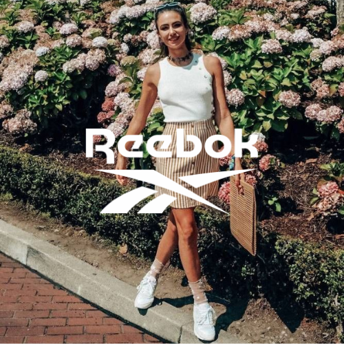 Reebok Kollektion – Frau vor Blumen stehend in Reebok Sneakern und Rock, sportlicher Lifestyle bei Closory